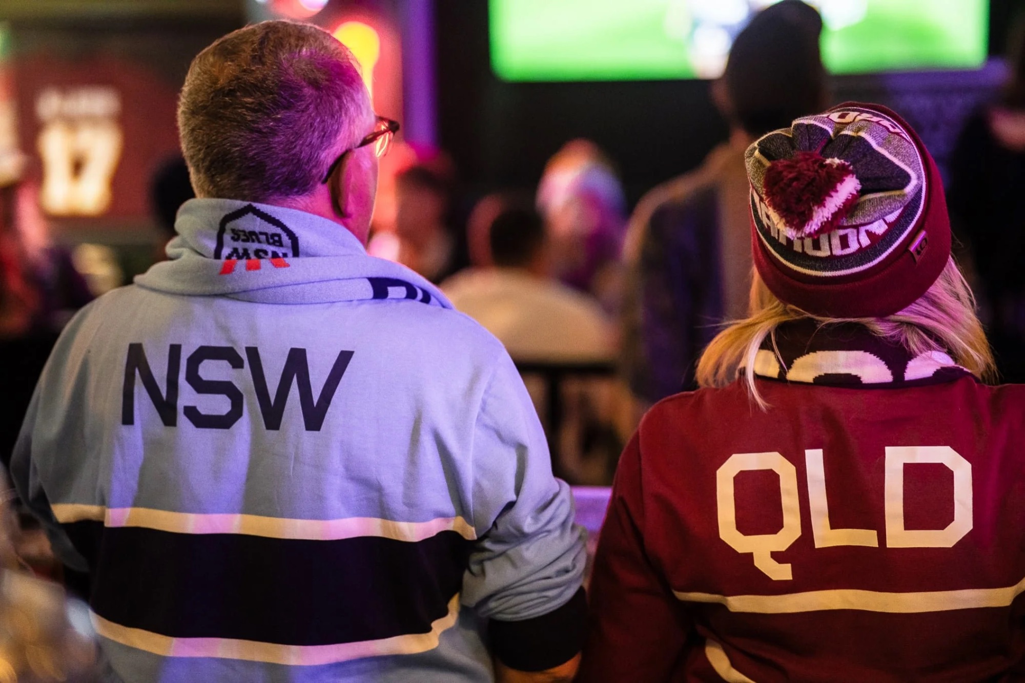 State of Origin fans in NSW and QLD jerseys watching the big screen