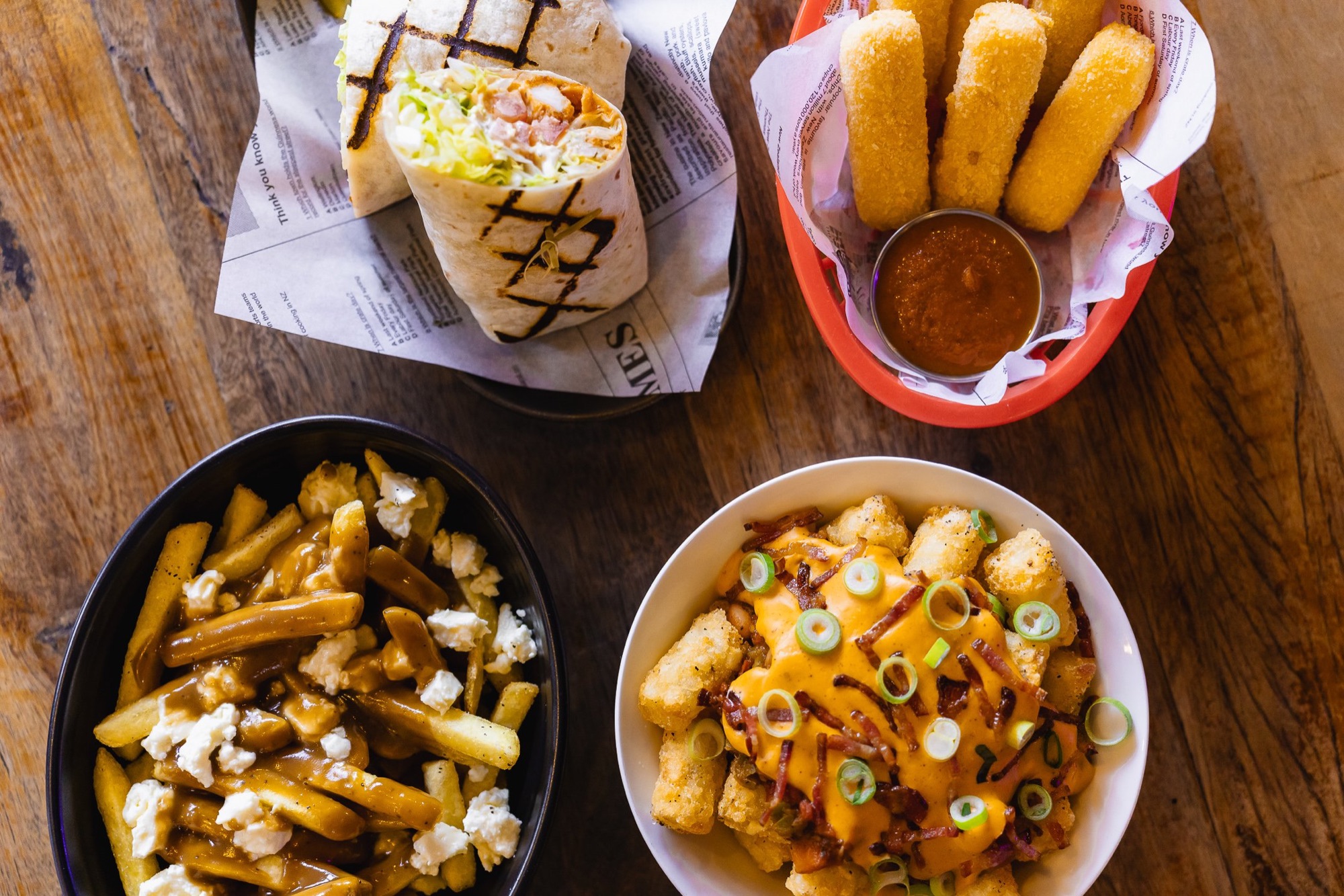 Wrap, mozzarella sticks, loaded tots and poutine-style fries on a table at The Locker Room