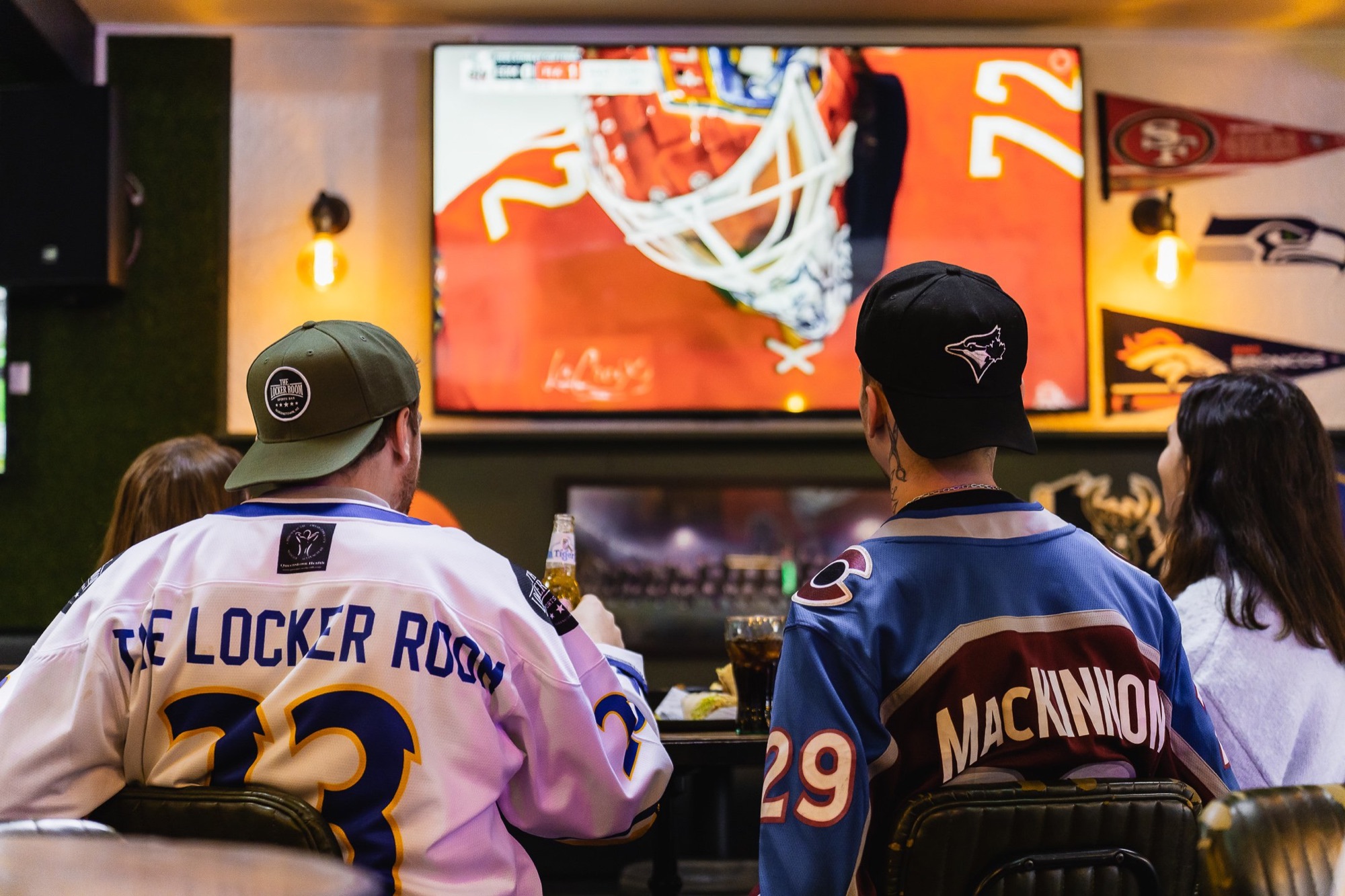 Fans in The Locker Room and Avalanche jerseys watching a game on the big screen