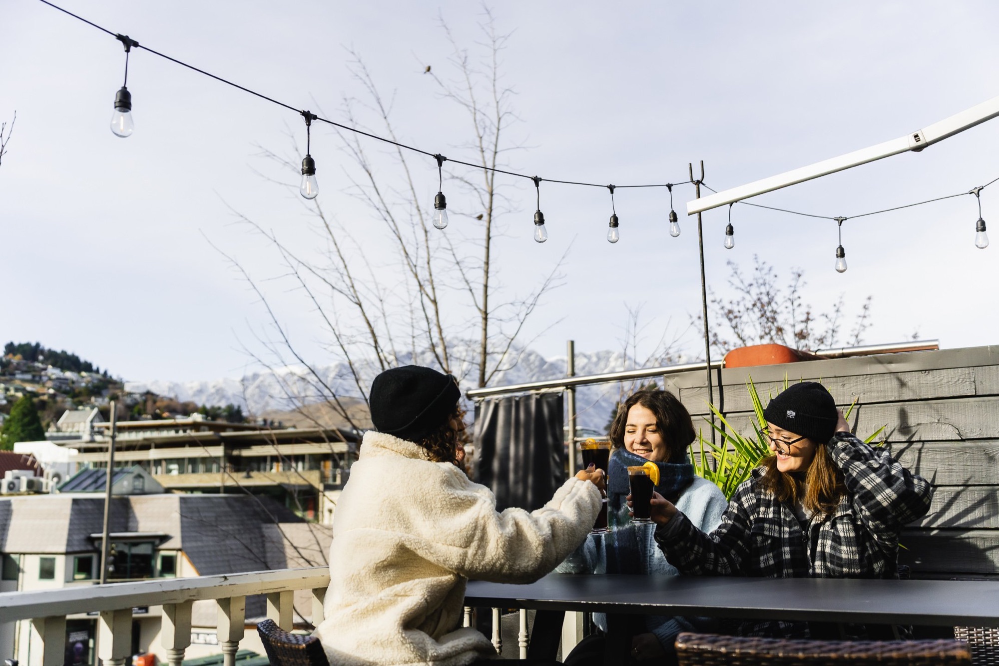 Friends toasting mulled wine on the rooftop with Queenstown mountain views