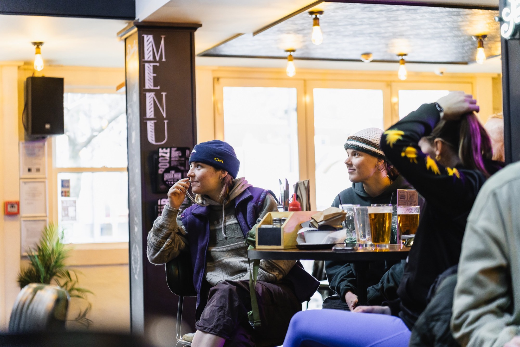 Friends seated near the menu board enjoying beers at The Locker Room