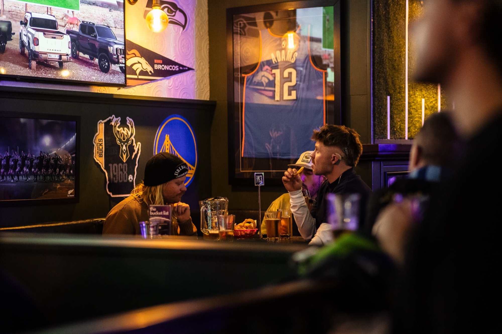Sports memorabilia and screens above patrons at The Locker Room