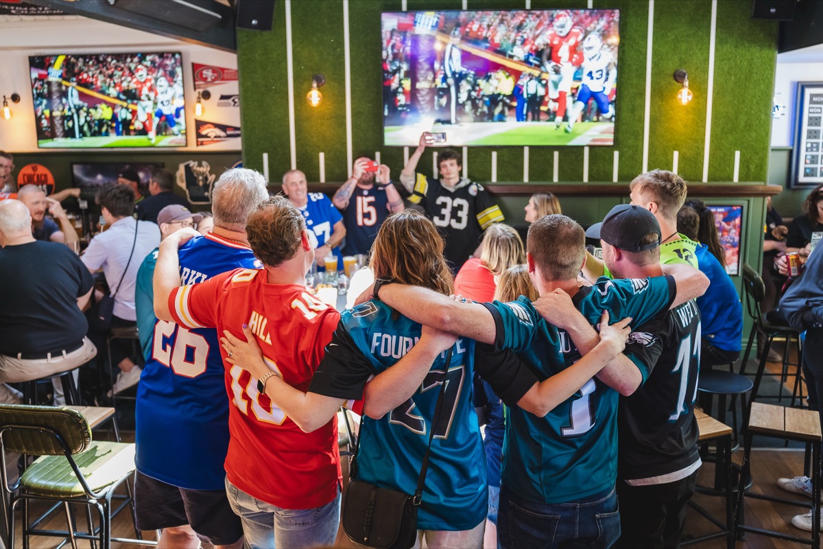 Fans in NFL jerseys watching a big game together at The Locker Room