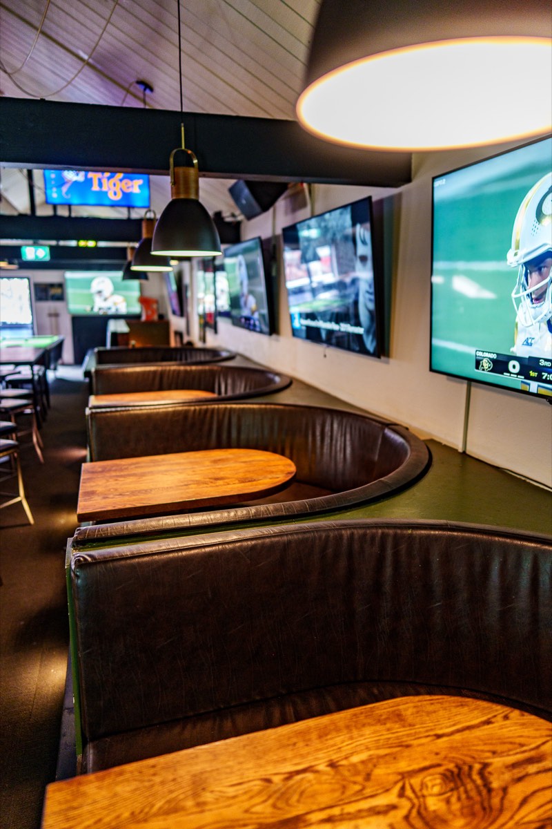 Row of curved booth seating with screens at The Locker Room
